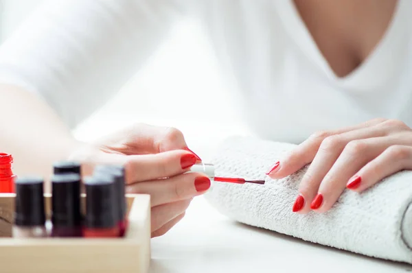 Jonge vrouw is haar nagels met rode nagellak schilderen — Stockfoto