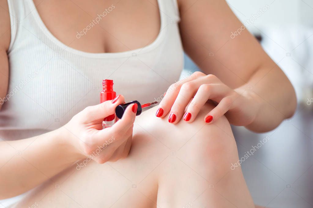 Young woman is painting her nails with red lacquer