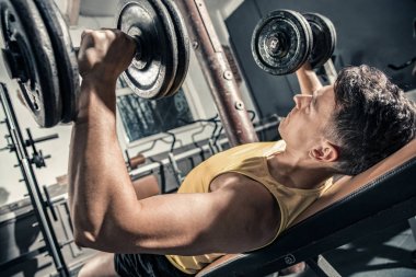 Genç sağlıklı adam göğsüne spor salonunda halter kaldırma trenler.