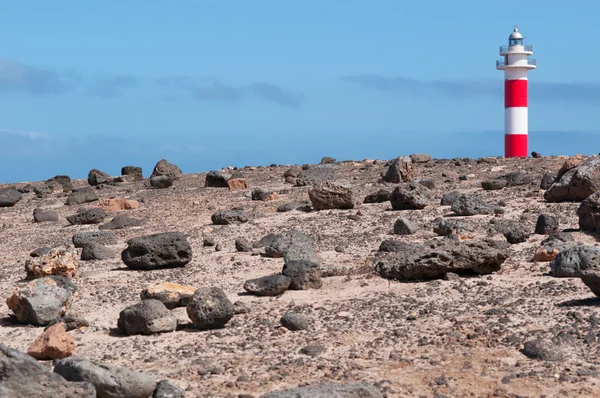 Fuerteventura, Canary Islands, Spain: black rocks and view of Faro de Toston (Toston lighthouse or El Cotillo lighthouse), an active lighthouse at Punta de la Ballena (Whale Point) whose original structure was opened in 1897 — Stock Photo, Image