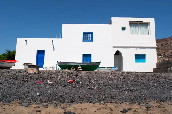 Fuerteventura, Canary Islands, Spain: the boats and a white house on the black beach of Pozo Negro, a fishing village away from touristic places whose black beach was created by lava flows millions years ago Royalty Free Stock Images