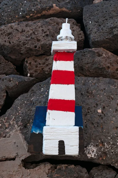 Un panel de madera con un faro colgado de rocas negras — Foto de Stock