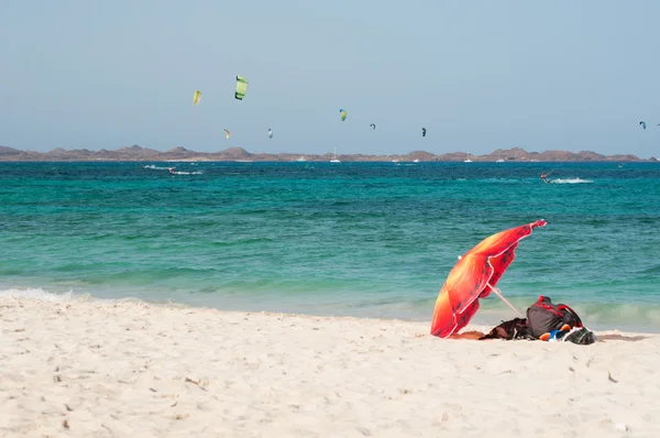 Fuerteventura, Islas Canarias, España: kitesurf y sombrilla en la playa de Grandes Playas, una de las famosas playas de kitesurf y windsurf, con vistas a la isla de Lobos, pequeña isla a 2 km al norte de Fuerteventura — Foto de Stock
