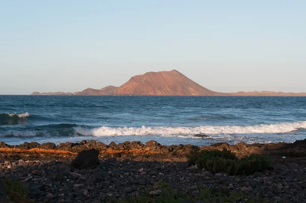 Fuerteventura, Canarische eilanden, Spanje: panoramisch uitzicht van Lobos eiland (Islote de Lobos), een klein eiland ligt slechts 2 kilometer ten noorden van het eiland Fuerteventura, gezien bij zonsondergang vanaf een rotsachtig strand in Corralejo — Stockfoto