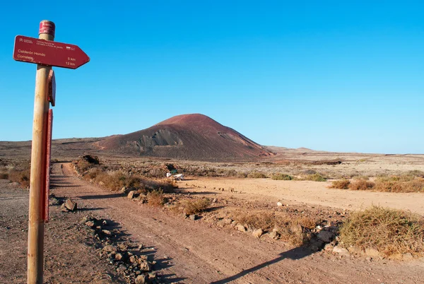 Fuerteventura, Kanári-szigetek, Spanyolország: a fa jelet naplementekor a gyalogút Calderon Hondo és Montana Colorada, kilátással a sziget Corralejo és Lajares közötti területen a két híres és színes vulkánok — Stock Fotó