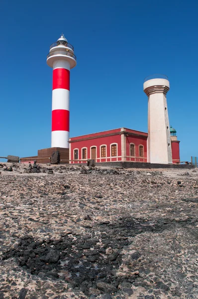 Fuerteventura, Kanárské ostrovy, Španělsko: černé skály a pohled na Faro de Toston (Toston maják nebo El Cotillo maják), aktivní maják na Punta de la Ballena (velryba bod) jejichž původní struktura byla otevřena v roce 1897 — Stock fotografie