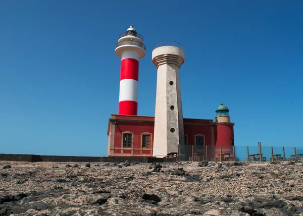 Fuerteventura, Kanárské ostrovy, Španělsko: černé skály a pohled na Faro de Toston (Toston maják nebo El Cotillo maják), aktivní maják na Punta de la Ballena (velryba bod) jejichž původní struktura byla otevřena v roce 1897 — Stock fotografie