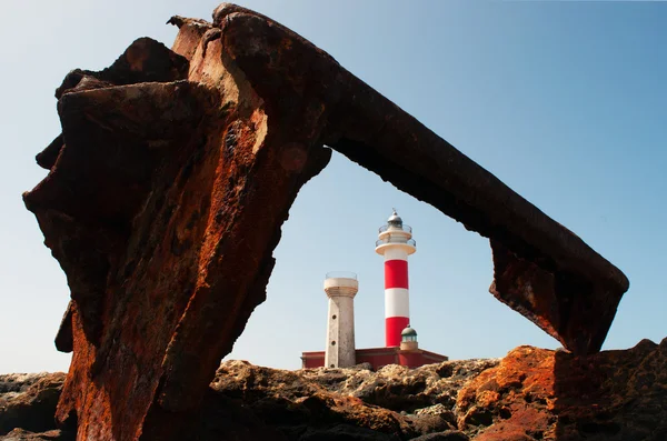 Fuerteventura, Islas Canarias, España: rocas negras con Faro de Toston (faro de Toston o faro de El Cotillo), un faro activo en Punta de la Ballena abierto en 1897, visto a través de los restos oxidados del naufragio de un barco — Foto de Stock