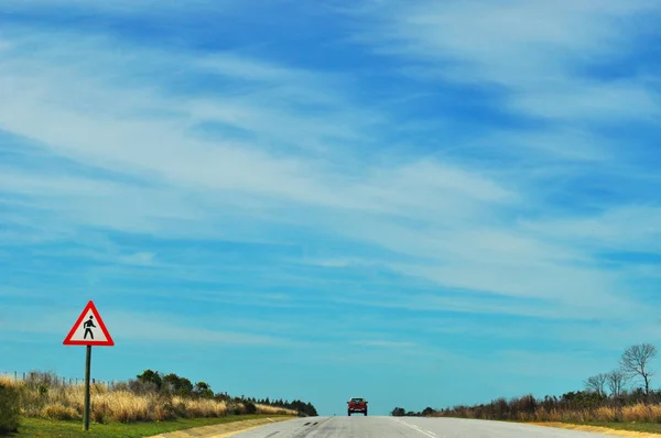 Zuid-Afrika: Waarschuwingsbord voor voetgangers oversteken van de N2, de Garden Route, de beroemde schilderachtige route van 300 kilometer, een stuk van groene vegetatie van de zuid-oostelijke kust van de West-Kaap tot de Oost-Kaap — Stockfoto