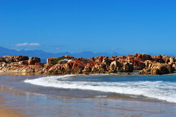 Sør-Afrika: bryte bølger og røde steiner på stranden ved Plettenberg Bay, kalt Plet or Plett, opprinnelig kalt Bahia Formosa (Vakker bukt), en by langs den berømte Garden Route – stockfoto