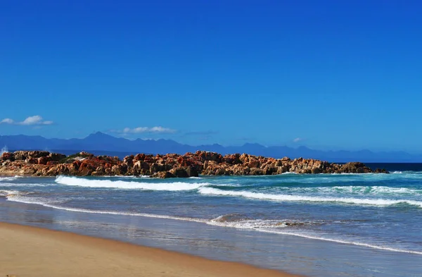 South Africa: breaking waves and red rocks on the beach of Plettenberg Bay, called Plet or Plett, originally named Bahia Formosa (Beautiful Bay), a town along the famous Garden Route — Stock Photo, Image