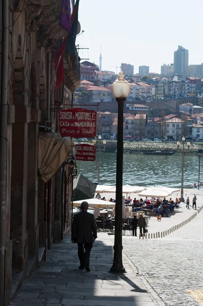 Porto : un lampadaire et un vieil homme marchant vers le centre de Praca da Ribeira, la place de la rivière, avec vue sur les enseignes des boutiques d'artisanat de la vieille ville — Photo