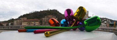 Spain: the Tulips, a bouquet of multicolor balloon flowers sculpture made by the artist Jeff Koons and located at the exterior of the Guggenheim Museum Bilbao, with view of the skyline clipart