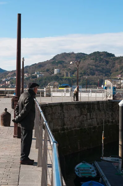 País Basco: um homem com a boina no porto com vista para o horizonte da Cidade Velha em frente ao mar de Donostia San Sebastian, a cidade costeira na Baía da Biscaia — Fotografia de Stock