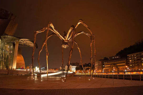 España: Maman, la gigantesca escultura de araña realizada por la artista Louise Bourgeois y situada en el exterior del Museo Guggenheim Bilbao, con vistas al horizonte nocturno de la ciudad — Foto de Stock