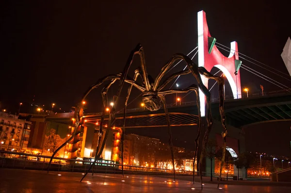 España: Maman, la gigantesca escultura de araña realizada por la artista Louise Bourgeois y situada en el exterior del Museo Guggenheim Bilbao, con vistas al horizonte nocturno de la ciudad — Foto de Stock