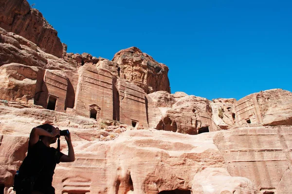 Jordânia: um homem tirando fotos da Rua das Fachadas, fileira de túmulos nabateu monumentais esculpidos na face sul do penhasco que fica além do Tesouro na cidade arqueológica de Petra — Fotografia de Stock