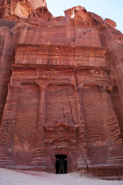 Jordânia: um homem e um túmulo vermelho ao longo da rua das fachadas, a linha de túmulos Nabataean monumental carved na cara do penhasco do sul que se encontra após o Tesouro na cidade archaeological de Nabataean de Petra — Fotografia de Stock