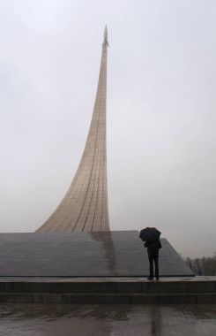 Moscow, Russia: man with umbrella in front of the Monument to the Conquerors of Space, a rocket on his launch ramp built in 1964 to celebrate achievements of the Soviet people in space exploration, inside whose base is the Museum of Cosmonautics  clipart