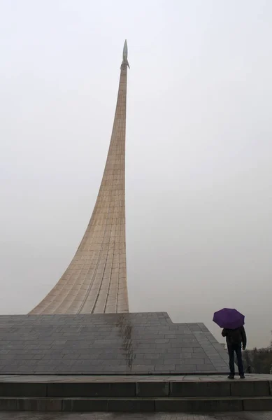 Moscou, Rússia: homem com guarda-chuva em frente ao Monumento aos Conquistadores do Espaço, um foguete em sua rampa de lançamento construída em 1964 para celebrar conquistas do povo soviético na exploração espacial, dentro cuja base é o Museu de Cosmonáutica — Fotografia de Stock