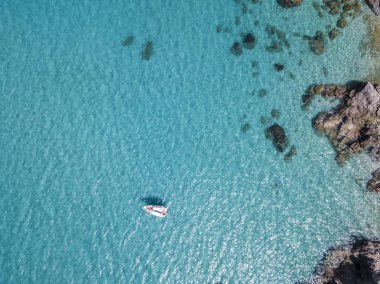 Havadan görünümü şeffaf bir denizde yüzen bir demirli teknenin. Dalış dinlenme ve yaz tatil. İtalyan kıyıları, plajları ve kayalar