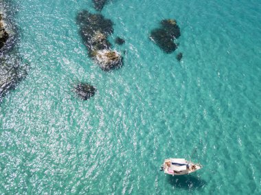 Havadan görünümü şeffaf bir denizde yüzen bir demirli teknenin. Dalış dinlenme ve yaz tatil. İtalyan kıyıları, plajları ve kayalar
