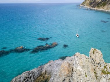 Havadan görünümü şeffaf bir denizde yüzen bir demirli teknenin. Denize bakan promontory ile plaj. Zambrone, Calabria, İtalya
