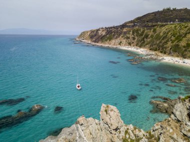 Havadan görünümü şeffaf bir denizde yüzen bir demirli teknenin. Denize bakan promontory ile plaj. Zambrone, Calabria, İtalya