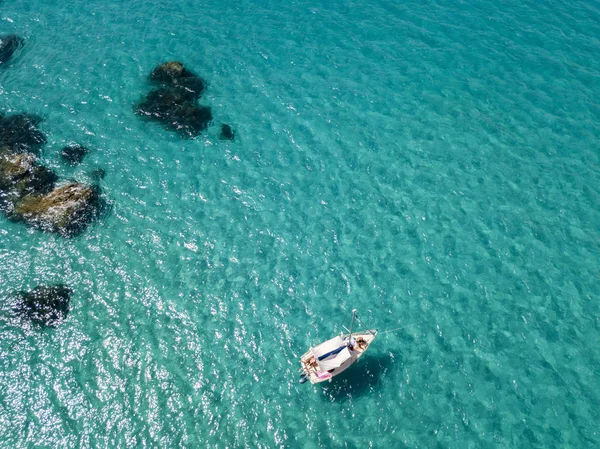Havadan görünümü şeffaf bir denizde yüzen bir demirli teknenin. Dalış dinlenme ve yaz tatil. İtalyan kıyıları, plajları ve kayalar