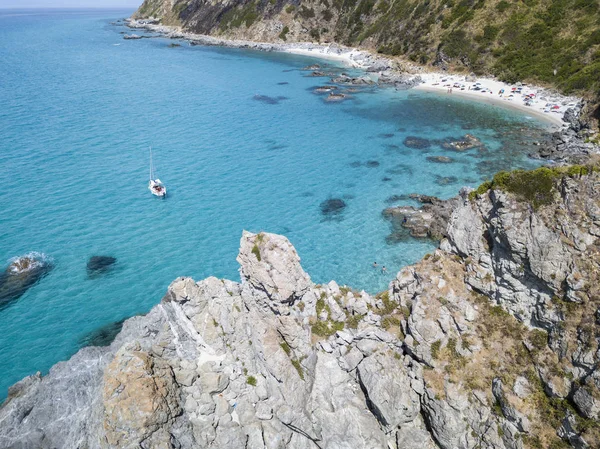 Havadan görünümü şeffaf bir denizde yüzen bir demirli teknenin. Denize bakan promontory ile plaj. Zambrone, Calabria, İtalya