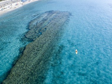 Aerial view of a canoe in the water floating on a transparent sea. Bathers at sea. Zambrone, Calabria, Italy. Diving relaxation and summer vacations. Italian coasts, beaches and rocks clipart