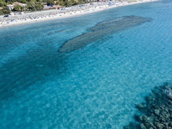 Вид с воздуха на каноэ в воде, плавающее на прозрачном море. Купающиеся в море. Замброне, Калабрия, Италия. Дайвинг релаксации и летних каникул. Итальянские побережья, пляжи и скалы — стоковое фото