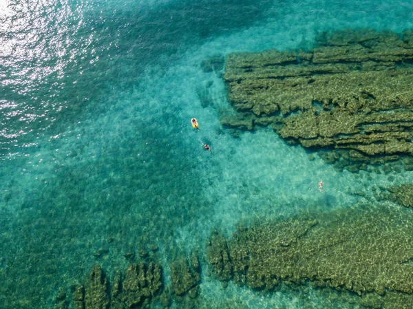 Aerial view of rocks on the sea. Overview of seabed seen from above, transparent water. Swimmers, bathers floating on the water — Stock Photo, Image