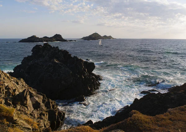 Corsica: rocks, waves and the Mediterranean Sea with view of the Iles Sanguinaires (Bloody Islands), the famous four dark red porphyry islands, a little archipelago in the Gulf of Ajaccio