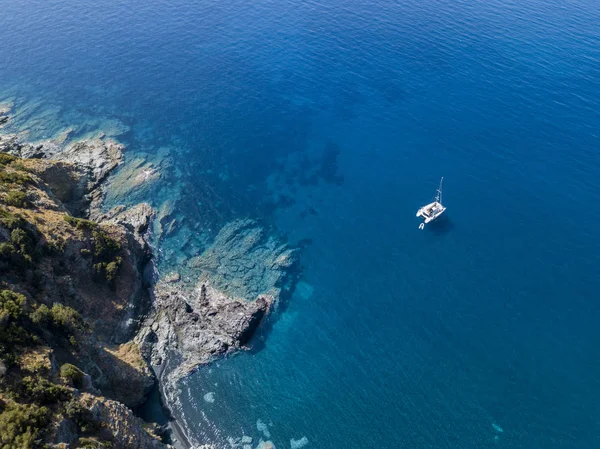 Deniz ve demirli bir katamaran tekne bakan sarp bir kayalığın hava görünümünü. Cap Corse Yarımadası, Corsica. Kıyı şeridi. Fransa