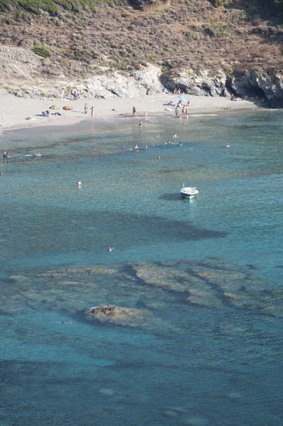 Córsega: um barco e pessoas nadando na água cristalina de Anse dAliso (Plage dAlisu), uma praia remota do lado oeste de Cap Corse, a península famosa por sua paisagem selvagem — Fotografia de Stock
