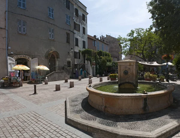Córcega: vista de la fuente de la plaza Doria en el centro de Saint-Florent, popular lugar de vacaciones de verano en la costa occidental conocida como el corse Saint-Tropez — Foto de Stock