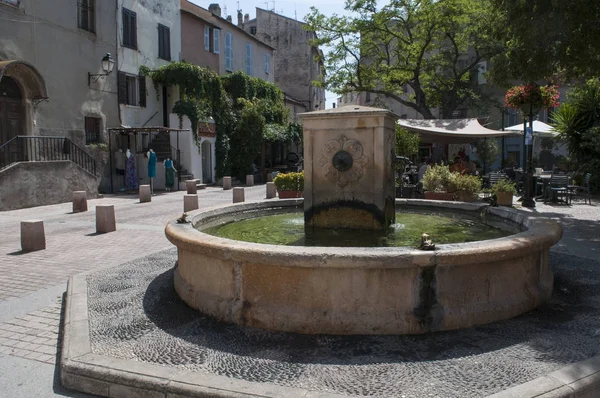 Córcega: vista de la fuente de la plaza Doria en el centro de Saint-Florent, popular lugar de vacaciones de verano en la costa occidental conocida como el corse Saint-Tropez — Foto de Stock