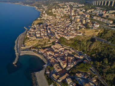 Pizzo Calabro, rıhtım, kale, Calabria, İtalya turizmi. Deniz kenarındaki küçük Pizzo Calabro kasabasının panoramik manzarası. Kayalıklardaki evler. Uçurumun kenarında Aragon kalesi duruyor. Gün batımında deniz önü