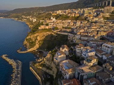 Pizzo Calabro, rıhtım, kale, Calabria, İtalya turizmi. Deniz kenarındaki küçük Pizzo Calabro kasabasının panoramik manzarası. Kayalıklardaki evler. Uçurumun kenarında Convento S. Francesco Di Paola duruyor. Gün batımında deniz önü