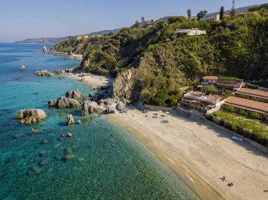 Tropea sahilinin hava manzarası, kristal berrak su ve sahilde ortaya çıkan kayalar. Calabria, İtalya. Yüzücüler, suda yüzen banyocular. Calabria kıyıları