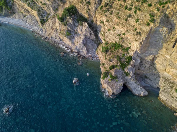 Aerial view of a steep cliff and a motor boat. Jagged coast on the Adriatic Sea. Cliffs overlooking the transparent sea. Wild nature and Mediterranean maquis