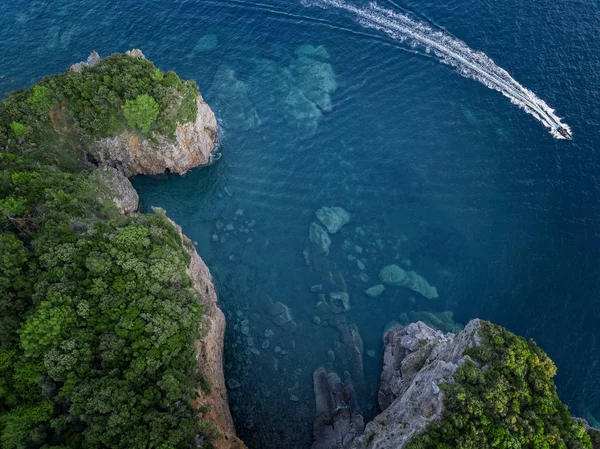 Aerial view of a steep cliff and a motor boat. Jagged coast on the Adriatic Sea. Cliffs overlooking the transparent sea. Wild nature and Mediterranean maquis