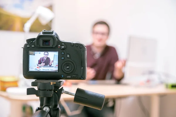 Camera on a tripod filming a blogger at home sitting on his workspace