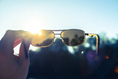 Adam elinde siyah kahverengi güneş gözlüğü, mavi gökyüzü güneş ışığı, akşam güneşi