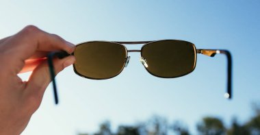 Adam elinde siyah kahverengi güneş gözlüğü, mavi gökyüzü güneş ışığı, akşam güneşi