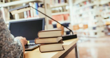 Sarışın kız öğrenci elinde kitap yığınıyla masada oturuyor, üniversite kütüphanesinde.