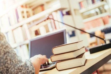 Sarışın kız öğrenci elinde kitap yığınıyla masada oturuyor, üniversite kütüphanesinde.