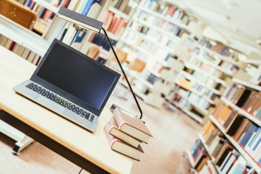 Dizüstü bilgisayar ve kitap yığını tahta bir masanın üzerinde. Üniversite kütüphanesi.