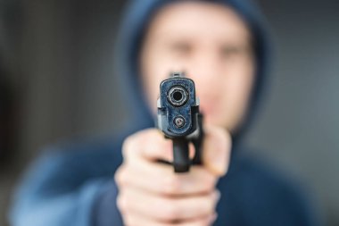 Soyguncu ya da suçlu siyah bir silahla nişan alıyor, yüzü bulanık.